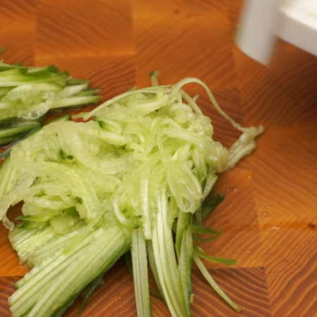 Сначала подготовим все ингредиенты для салата.
Один свежий огурец разрезаем пополам. Каждую часть огурца трем на терке для корейской морковки.