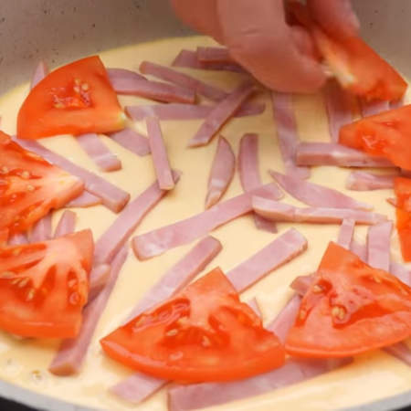 Сразу же на тесто выкладываем нарезанную колбасу. На колбасу кладем пластинки помидора.