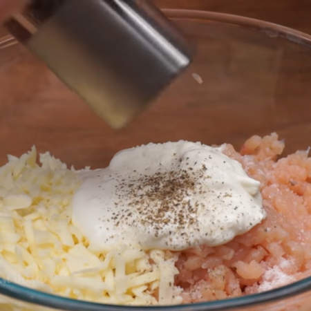 В миску с подготовленным фаршем кладем тертый сыр и добавляем 100 г сметаны. Сметану можно заменить кефиром.
Фарш солим примерно половиной ст. л. соли и перчим по вкусу.