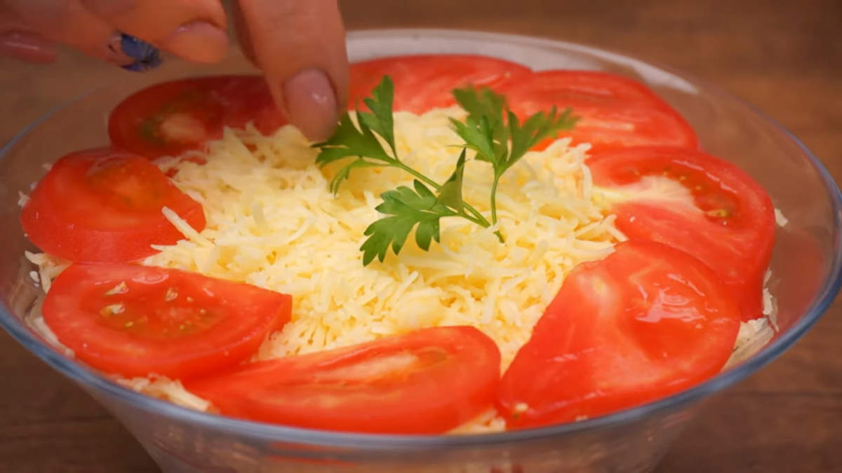 В самом конце, на сырный слой выкладываем по кругу пластинки помидоров, В центр насыпаем еще немного тертого сыра. Салат украшаем листиками петрушки.
Салат готов, можно подавать на стол.
