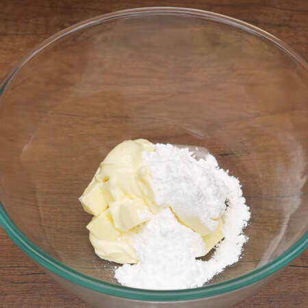 В сухую миску кладем 200 г размягченного сливочного масла и засыпаем оставшуюся часть сахарной пудры.