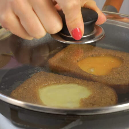 Сковороду накрываем крышкой и жарим яйца на самом маленьком огне до готовности.