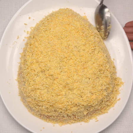 И последним слоем кладем тертый желток. Желтком равномерно покрываем весь салат, снизу желток приминаем ложкой, придавая салату форму яйца.
