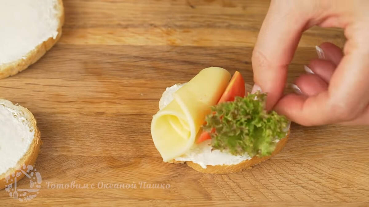 С одной стороны бутерброда кладем скученный цветок из сыра, возле него, посередине, ставим дольку помидора. С другой стороны бутерброда кладем скрученные листья салата. Так готовим все бутерброды.
