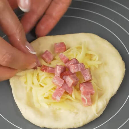 На вторую половину пирожков кладем тертый сыр и сверху выкладываем нарезанную колбасу.
