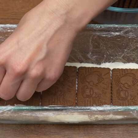 На него выкладываем слой шоколадного песочного печенья. Когда выкладываете печенье, старайтесь, чтобы оно не касалось бортиков формы, чтобы торт получился с белыми красивыми боками. Снова кладем крем. Выкладываем слой из печенья. Если целое печенье не помещается, то разрезаем его по размеру с помощью ножа. 