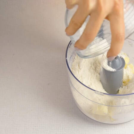 Пока запекается тыква приготовим тесто. Масло, нарезанное на кусочки кладем в чашу измельчителя.  Сюда же насыпаем муку. 