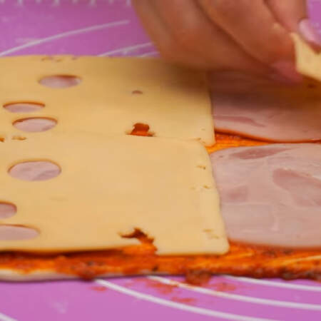 На соус выкладываем тонко нарезанную колбасу. Сверху на колбасу кладем пластинки сыра. На 2 листа слоеного теста понадобится 200 г колбасы и 300 г сыра.