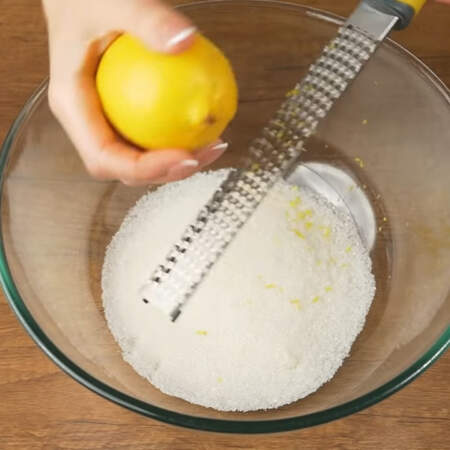 Сначала замесим тесто.
В миску насыпаем 130 г сахара. С двух лимонов снимаем цедру с помощью терки, снимаем только верхний желтый слой.