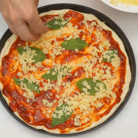 Сделаем пиццу маргарита. Тесто смазываем заранее подготовленным соусом или кетчупом. На соус кладем листочки базилика и посыпаем тертым сыром.