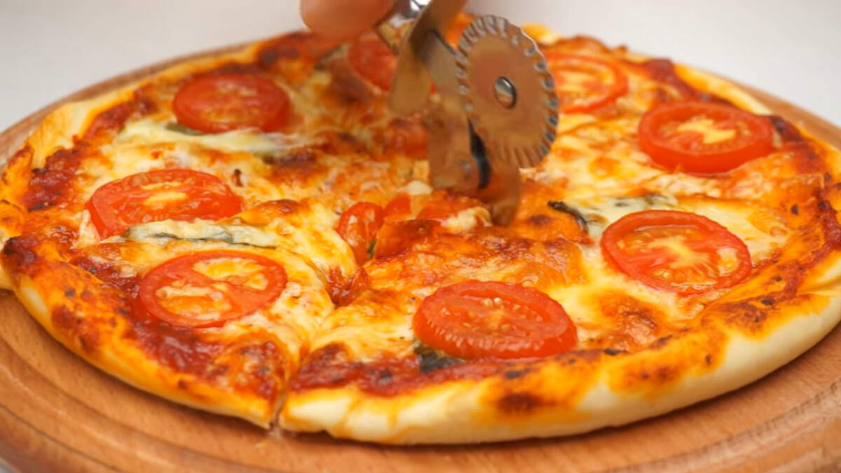 Готовую пиццу перекладываем на доску и пока еще горячая, разрезаем ее на порционные куски.