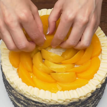 Дольки персиков выкладываем сверху торта. Начинаем с внешней стороны. Выкладываем их по кругу имитируя цветок. Для украшения торта понадобилась 1 банка консервированных персиков.

