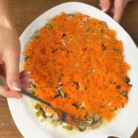 Следующим слоем кладем тертую морковь. Распределяем ее по всей поверхности салата.