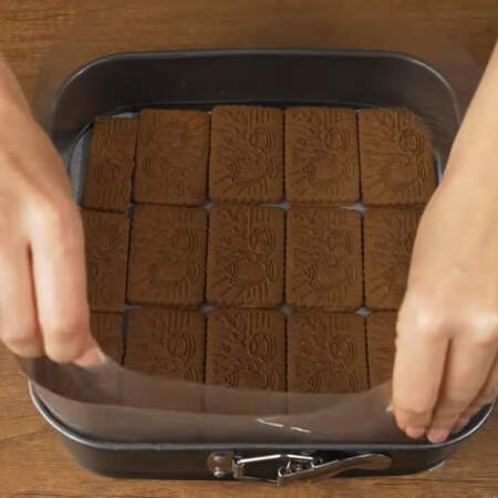 На дно формы выкладываем в один слой шоколадное песочное печенье. Если нужно, печенье подрезаем по размеру. По бокам формы ставим ацетатную пленку. Размер моей формы 23 см * 23см.
