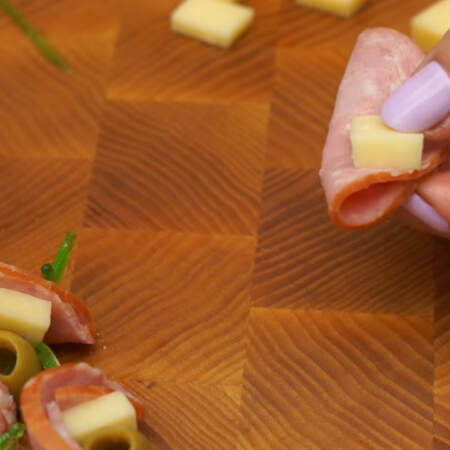 Пластинку колбасы складываем пополам. На нее кладем кусочек сыра и одну оливку. Все прокалываем шпажкой. 