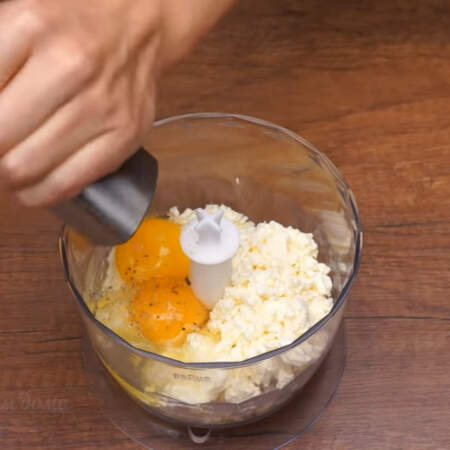 Подготовленный сыр кладем в чашу измельчителя, сюда же добавляем 100 г творога и разбиваем 2 яйца. Начинку солим по вкусу и перчим.