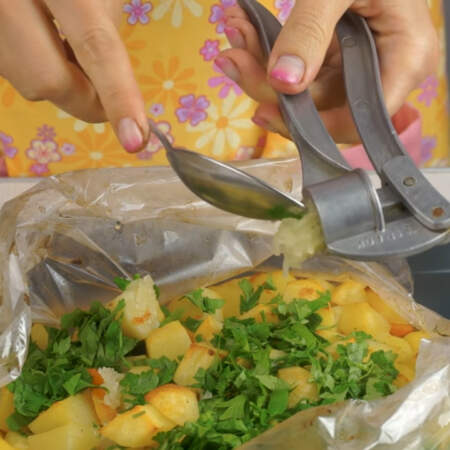 Готовый картофель достаем из духовки и аккуратно разрываем рукав сверху.  На картофель высыпаем измельченную зелень и выдавливаем через пресс 2 зубчика чеснока. 