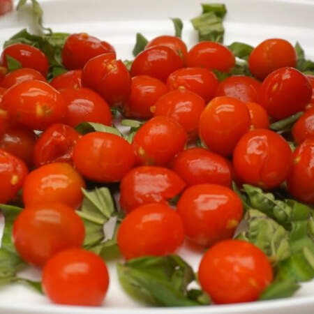 На дно блюда в котором будем подавать салат на стол кладем нарезанные листья базилика.
Затем выкладываем раздавленные помидоры черри. 
