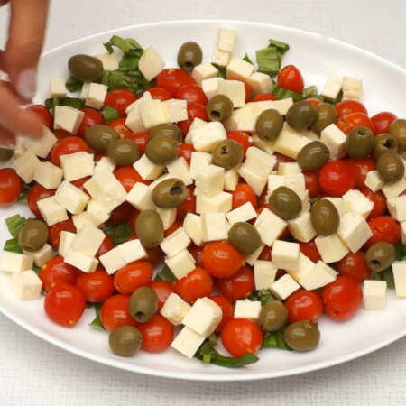 На помидоры кладем нарезанный кубиками сыр. И сверху салата выкладываем одну банку зеленых оливок без косточки.
