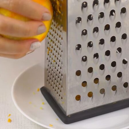 Сначала подготовим апельсин и изюм. С апельсина снимаем цедру. Снимаем на мелкой терке только оранжевую часть кожуры.