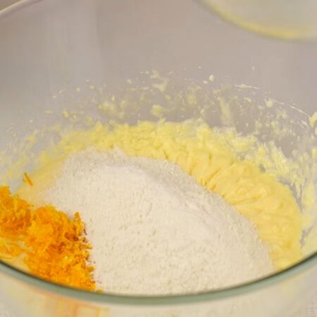 В тесто высыпаем подготовленную цедру апельсина и сюда же добавляем перемешанную муку с разрыхлителем примерно в три подхода. 