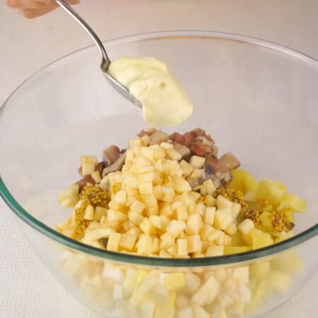 В миску кладем нарезанный картофель, яйца, селедку и яблоки. Все немного солим. Салат-закуску заправляем 2 ч. л. горчицы в зернах и 1 ст. л. майонеза. Все перемешиваем. 
