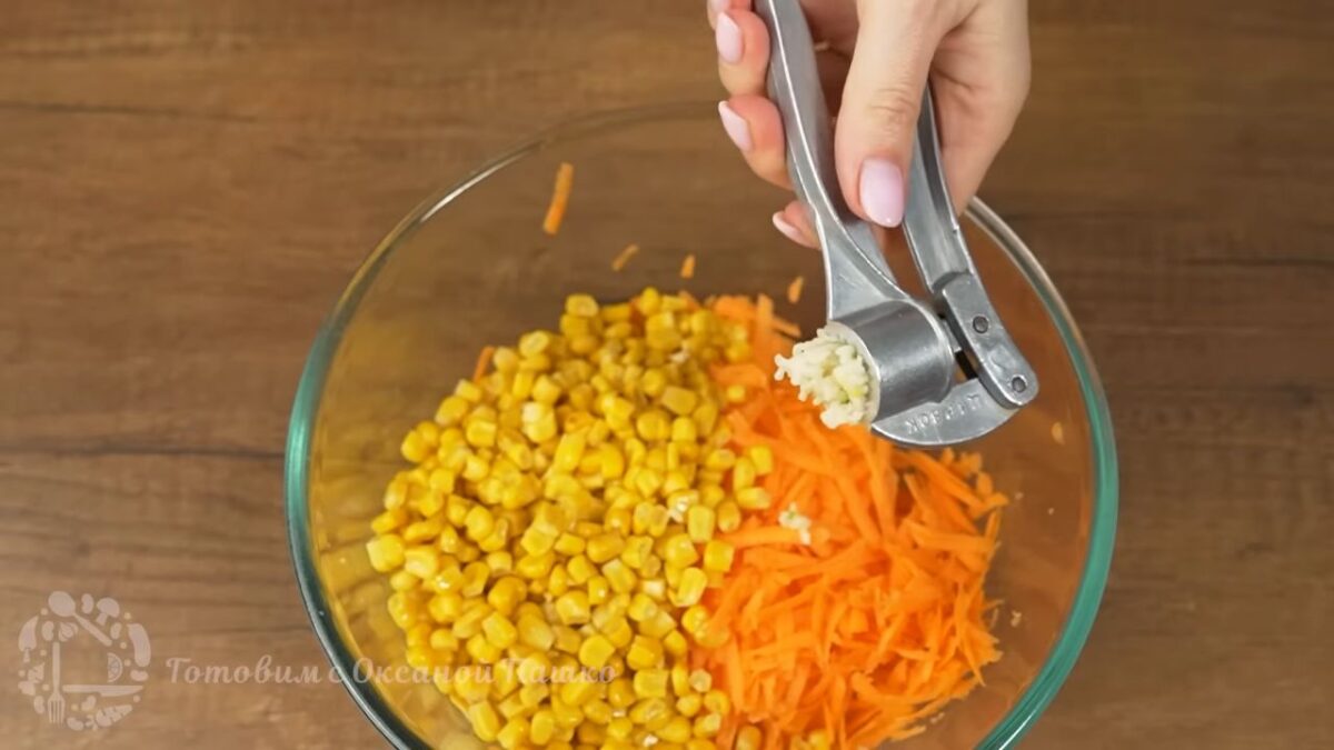К моркови добавляем 1 банку консервированной кукурузы.
Сюда же выдавливаем 2 зубчика чеснока через пресс.
Салат немного солим.
