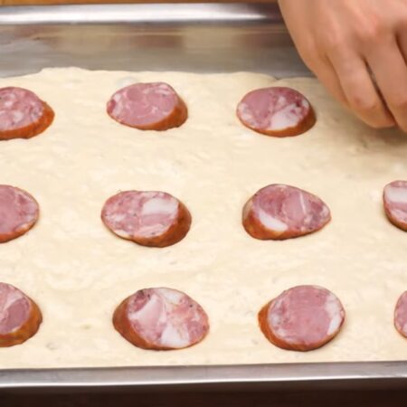 На тесто выкладываем нарезанные кусочки колбасы. Выкладываем так, чтоб потом, при нарезке пирога на квадраты, в центре каждого кусочка была колбаса.