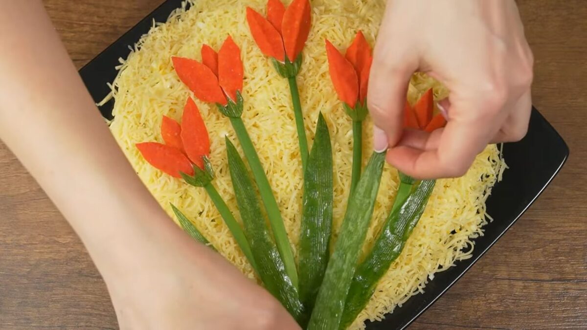 Готовые чашелистики выкладываем под каждым цветком.
По салату раскладываем листья тюльпанов из огурца.
Салат готов, можно подавать на стол.
