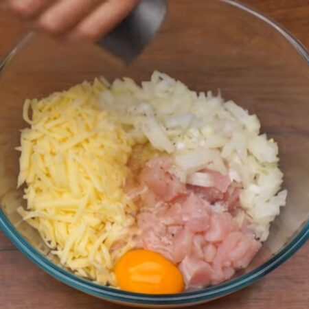 В миску кладем подготовленное филе, сыр и нарезанный лук. Сюда же разбиваем 1 яйцо, солим по вкусу и перчим.