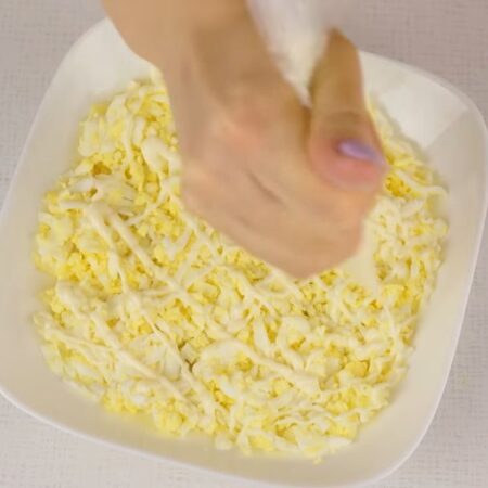Вторым слоем выкладываем половину тертых яиц. Яйца немного солим и наносим сеточку из майонеза.
