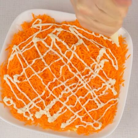 Третьим слоем кладем половину тертой моркови. Морковь тоже немного солим и наносим майонез.