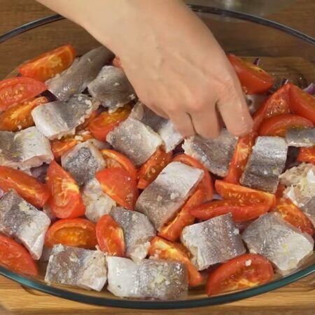 Овощи немного запеклись, достаем их из духовки. 
Между помидорами кладем кусочки маринованной рыбы. Оставшийся маринад тоже выливаем в форму.