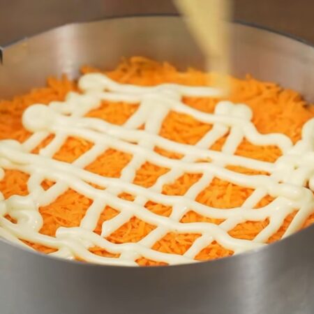 Следующим слоем кладем тертую морковь, распределяем ее по салату. Немного солим и утрамбовываем ложкой. Наносим майонез.