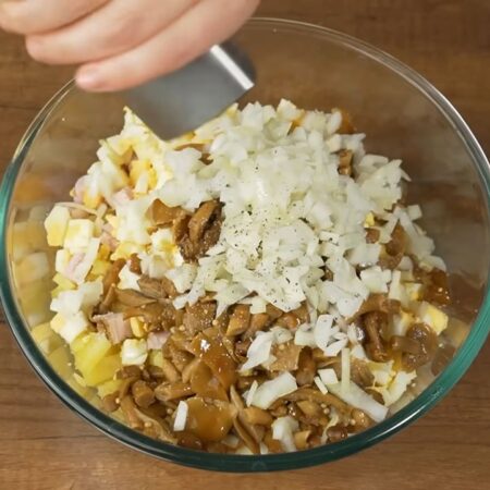 В миску насыпаем подготовленный картофель, ветчину, морковь, нарезанные яйца, грибы и маринованный лук. Салат немного солим и перчим черным молотым перцем. 
