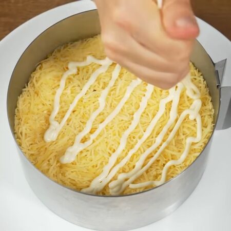На колбасу выкладываем слой из тертого сыра. Распределяем его и утрамбовываем. Наносим майонез.