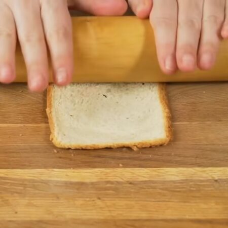 Сначала подготовим хлеб.
Кладем кусочек хлеба на доску и раскатываем его скалкой. Для этой закуски хорошо подходит тостерный хлеб. Если хлеб не достаточно мягкий, плохо раскатывается и крошится, положите его в микроволновку на несколько секунд, чтобы он стал теплым и мягким. Я ставлю греться сразу по 2 кусочка на 10 секунд.