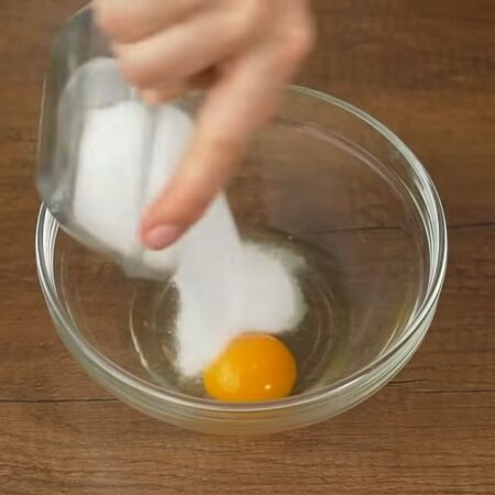 В отдельную миску разбиваем 1 яйцо, насыпаем щепотку соли, добавляем 10 г ванильного сахара и 100 г сахара. 
