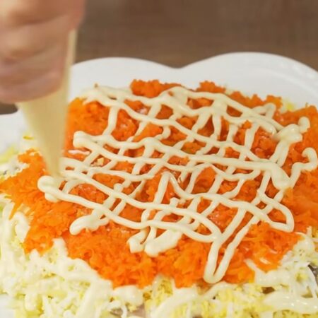 Следующим слоем кладем всю тертую морковь. Распределяем по салату, немного солим. Наносим сеточку из майонеза.
Все ингредиенты стараемся выложить полукруглой горочкой.
