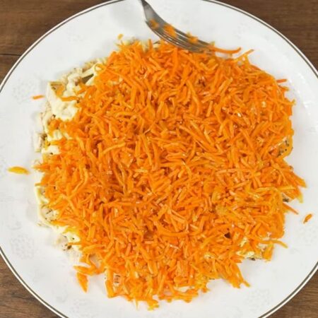 Следующим слоем на салат выкладываем подготовленную морковь. Равномерно распределяем ее по мясу. Вместо морковки по-корейски можно использовать свежую или вареную тертую морковь.
