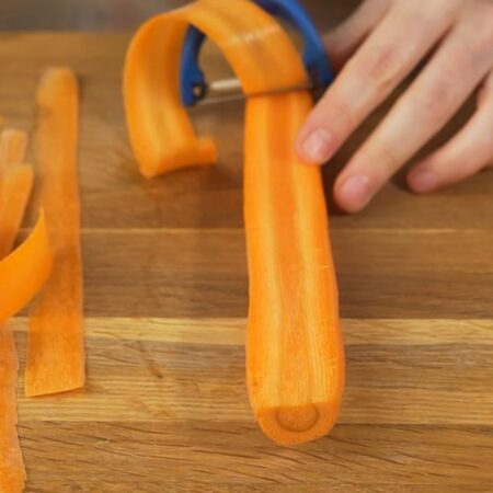 Начнем с подготовки моркови для украшения, так как ей нужно постоять около двух часов. Берем длинную морковь и нарезаем ее тонки пластинками. Это лучше всего делать овощечисткой. Ножом настолько тонкие пластинки не получится нарезать. В процессе нарезки морковь через каждые 3-4 полоски разворачиваем.